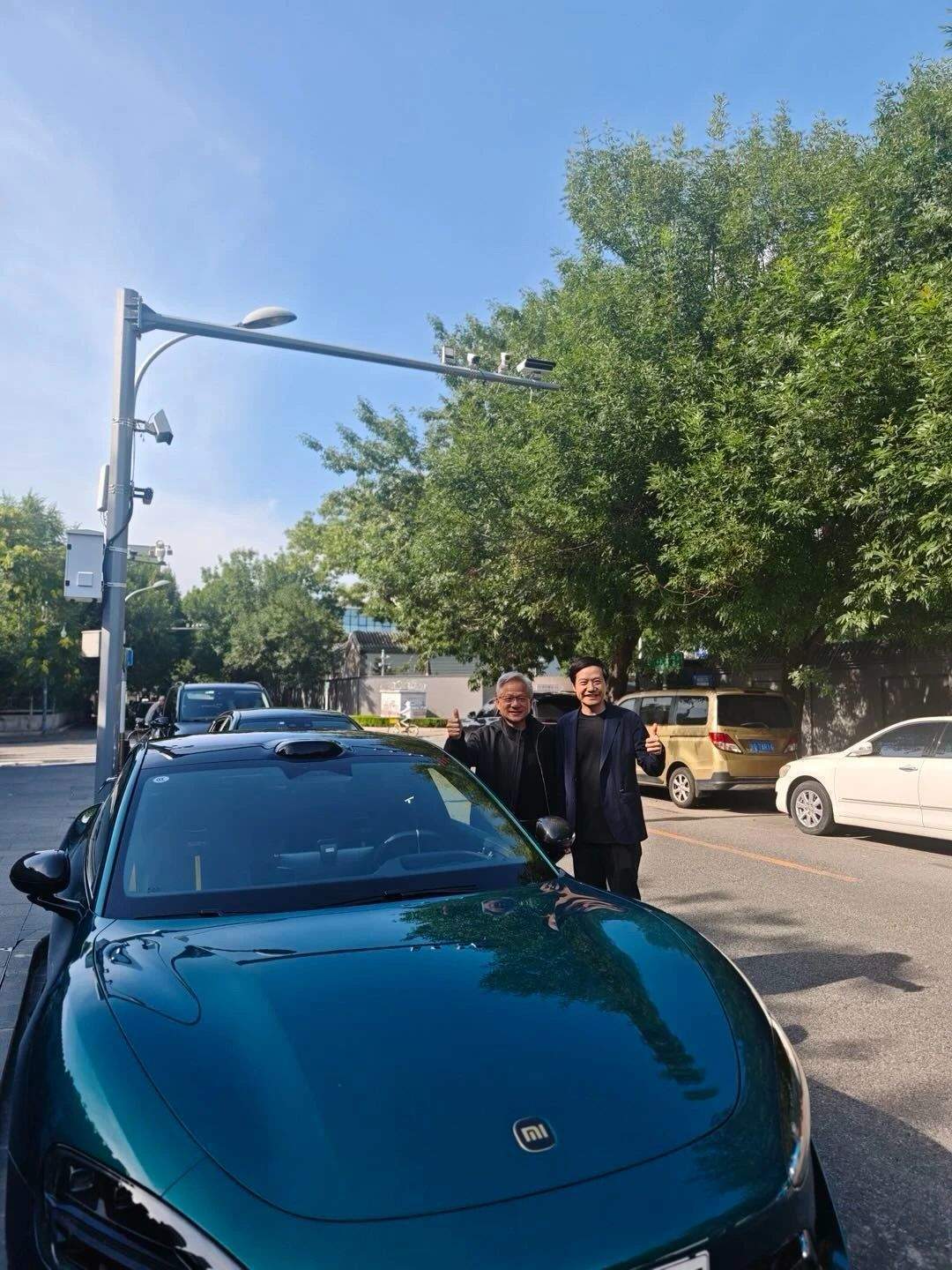 黄仁勋与雷军合影，35度天气仍穿皮衣！两人站在一辆小米汽车前，面带微笑，显得十分亲切